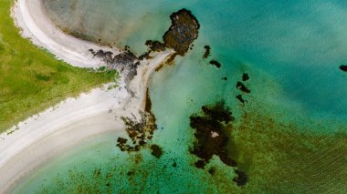 Turkuaz suların yemyeşil çimenler ve beyaz kumla buluştuğu kayalık bir çıkıntının etrafında kıvrılan el değmemiş bir sahil manzarası. Kolbedeliden Sahili, Lofoten