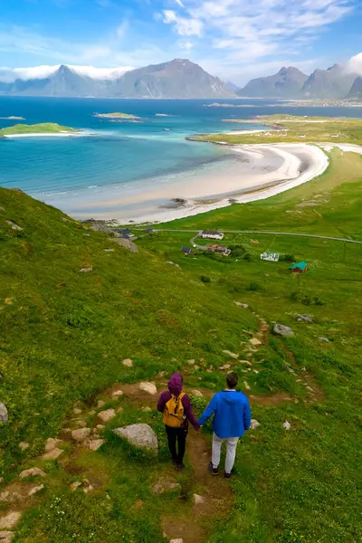 stock image A couple walks hand-in-hand along a grassy path overlooking a breathtaking Norwegian beach. Kolbeinsanden Beach, Lofoten