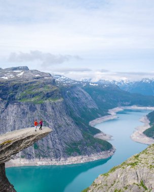 Norveç, Trolltunga 'da bir çift, Norveç' te manzaralı bir fiyorda bakan bir uçurumun kenarında duruyor. Norveç, Trolltunga 'da bir dağın tepesinde bir kadın ve erkek.