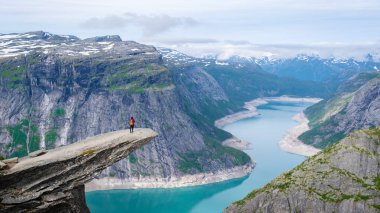 Norveç 'teki Trolltunga uçurumunun kenarında tek başına yürüyen bir yürüyüşçü, geniş, mavi bir fiyorda bakıyor. Norveç, Trolltunga 'da Asyalı kadınlar