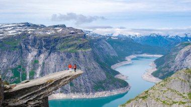 Norveç, Trolltunga 'nın kıyısında iki yürüyüşçü duruyor. Norveç' te muhteşem bir fiyorda bakan devasa bir uçurum. Manzaranın enginliği ve katıksız damlası nefes kesici bir manzara yaratır..