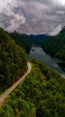 Sarmal bir yol yemyeşil bir vadi boyunca kıvrılır, sisle kaplanmış yüksek dağların arasına yerleşir. Sakin sahne, Norveç 'in doğal manzarasının dramatik güzelliğini gözler önüne seriyor. Lovrafjorden