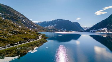 Manzaralı bir yol yemyeşil dağların arasından esiyor ve Norveç 'te ışıl ışıl mavi bir gölü geçiyor. Langvatnet, Geiranger, Norveç