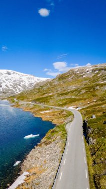 Norveç 'teki dağlık bir arazide bir yol kıvrılır, aşağısı mavi bir göl ve uzaktan karlı zirveler. Strynefjellsvegen, Geiranger, Norveç