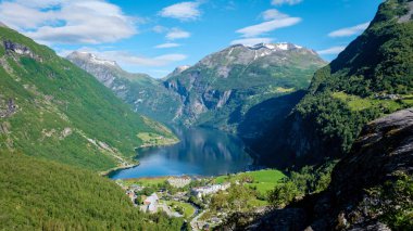 Geiranger Fjord Norveç, yemyeşil dağlarla çevrili bir Norveç fiyortunun göz kamaştırıcı manzarası, aşağıdaki vadide küçük bir kasaba var..