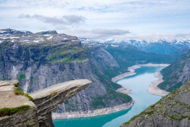 Trolltunga 'dan nefes kesici bir manzara, Norveç' te bir uçurum, dolambaçlı mavi bir göle ve karla kaplı dağlara bakıyor. Trolltunga, Norveç,
