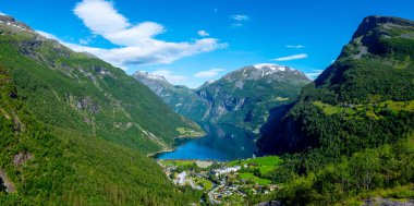 Resimli bir köy, Norveç fiyortlarının dingin sularına yuva yapmış, yüksek yeşil dağların eteğinde yer alır. Geiranger Fjord Norveç