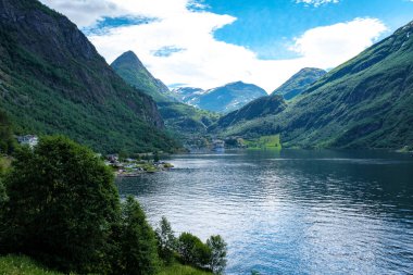Norveç 'te muhteşem bir fiyort manzarası, her iki tarafında yüksek yeşil dağlar ve ön planda sakin, mavi bir su kütlesi. Geiranger Fjord Norveç