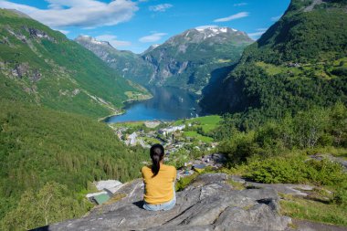 Soluk kesici Norveç fiyorduna tepeden bakan kayalık bir çıkıntıda oturan bir kadın yeşil dağların ve mavi suların güzelliğini içine çekiyor. Geiranger Fjord Norveç