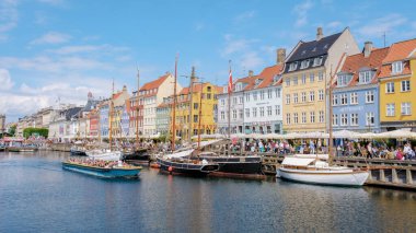 Kopenhag Danimarka 21 Temmuz 2024, Kopenhag, Danimarka 'da renkli binalarla dolu hareketli bir kanal. İnsanlar yaz gününün tadını çıkarıyor, tekneler ve yelkenliler geçiyor..