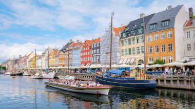 Kopenhag Danimarka 21 Temmuz 2024 'te Kopenhag, Danimarka' da bir kanal boyunca parlak renkli bir grup tekne denize açıldı. Kanal boyunca uzanan binalar sarı, kırmızı ve mavilerin canlı bir karışımıdır..