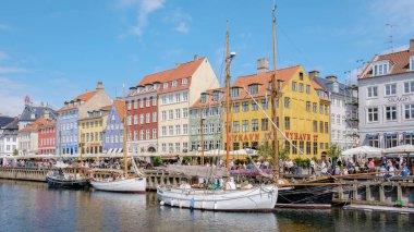 Kopenhag Danimarka 21 Temmuz 2024, Kopenhag Nyhavn 'da güneşli bir gün, rıhtımda parlak boyanmış binalar var. Yelkenliler rıhtıma yanaştı ve insanlar kaldırım taşı caddelerinde geziniyor..