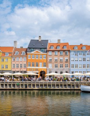 Kopenhag Danimarka 21 Temmuz 2024, Kopenhag, Danimarka 'da bir kafede güneşli bir günün tadını çıkarıyorlar. Renkli binalar büyüleyici bir zemin oluşturuyor..