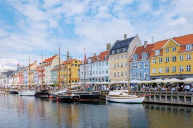 Kopenhag Danimarka 21 Temmuz 2024, Kopenhag, Danimarka 'da renkli binaların bulunduğu canlı bir manzara. Tekneler rıhtıma yanaştı ve insanlar kafelerin dışında güneşli bir günün tadını çıkarıyorlar..