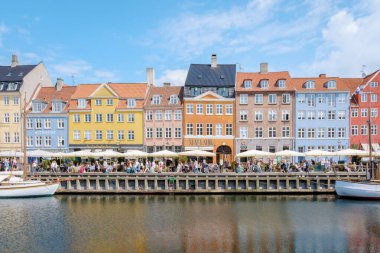 Kopenhag Danimarka 21 Temmuz 2024, Rıhtımda hareketli bir kafe sahnesi başlıyor, renkli binalar kanalı kaplıyor ve müşteriler güneşli gökyüzünün altında içki içip sohbet ediyorlar..