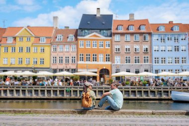 Kopenhag 'da kanalın kenarında oturan iki kişi gün ışığının ve renkli binaların manzarasının tadını çıkarıyorlar. Kopenhag Danimarka 