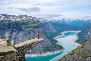 Norveç, Trolltunga 'nın kıyısında bir çift duruyor. Norveç' te ünlü bir uçurum. Çevreleyen dağların nefes kesici manzarasına ve dolambaçlı bir göle bakıyor..
