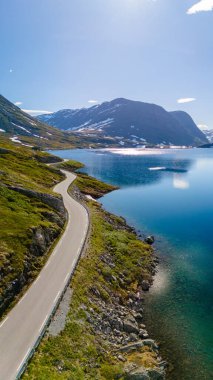 Göz kamaştırıcı Norveç manzarası boyunca uzanan manzaralı bir yol, kristal berrak bir göl boyunca uzanan, karla kaplı dağlarla çevrili. Langvatnet, Geiranger, Norveç