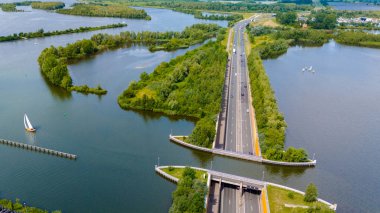 Hollanda 'daki Aquaduct Veluwemeer' in hava görüntüsü, bir su kanalının altından geçen bir otoyolu gösteriyor. Orman adasında yelkenli botlarla, yakındaki sularda bir yelkenliyle..