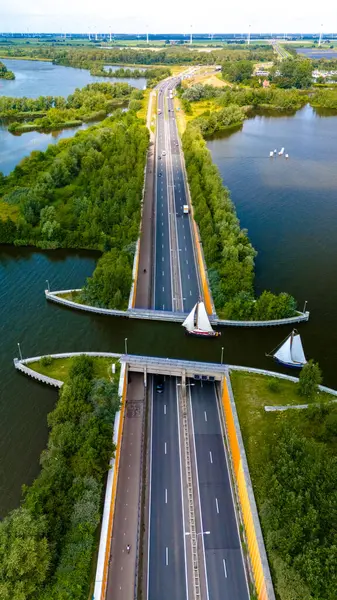 stock image An aerial view of the Aquaduct Veluwemeer in the Netherlands. The highway bisects a canal, with sailboats navigating through the opening. Lush greenery borders the road and waterways.