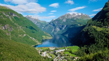 Yeşil yemyeşil dağlarla çevrili bir Norveç fiyordunun su kenarına kurulmuş küçük bir köyünün çarpıcı manzarası. Geiranger Fjord Norveç