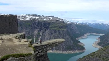 Bir dağın yamacında duran, göle ve doğal manzaraya hayran bir insan. Anahtar sözcükler Su, Gökyüzü, Doğa, Dağ, Bulut, Seyahat, Göl, Peyzaj, Trol Tunga, Norveç