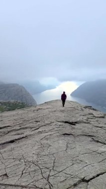 Bir insan yüksek kayalıklardan ve tepelerden manzaralı manzaralar izler aşağıdaki güzel su ve vadileri seyreder, gökyüzü ile çevrili, Preikestolen Norveç