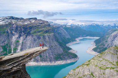 Norveç 'teki Trolltunga uçurumunun kenarında duran bir çift fiyortun çarpıcı mavi sularına bakıyor. Norveç 'teki Trolltunga Dağı' nın kıyısında bir çift kadın ve erkek.