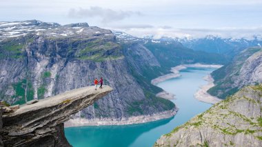 Norveç 'in Trolltunga şehrinin kıyısında, Norveç' in sakin gölüne ve etrafındaki dağlara bakan bir uçurumda iki kişi duruyor. Norveç 'te bir dağın tepesinde bir çift kadın ve erkek.