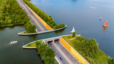 Hollanda 'daki Aquaduct Veluwemeer' in hava görüntüsü, üzerinde tekneler olan bir su yolunu geçen bir otoyolu gösteriyor..