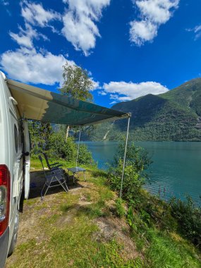 A peaceful camping setup near sparkling waters, with mountains in the background and a clear sky enhancing the serene atmosphere. clipart