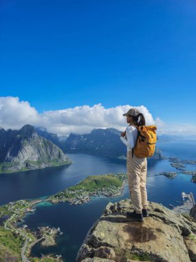 Bir gezgin kayalık bir çıkıntının tepesinde durur, büyüleyici fiyortlara ve Lofoten adalarına hayran kalır, güneş ışığıyla yıkanır. Reinebringen Lofoten Norveç 