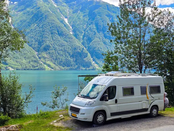 Çekici bir karavan Norveç 'te berrak bir gökyüzünün altında yemyeşil dağlarla çevrili sakin mavi sularda park halinde..