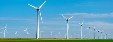 Dev rüzgar türbinleri Hollanda 'da zarifçe dönerek temiz enerji üretirken gölgeler canlı yeşil alanlar üzerinde dans ediyor. Bir Hollandalı hendeğin yanındaki yel değirmeni parkı.