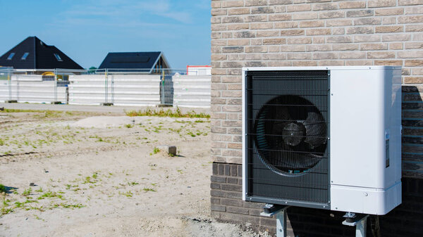 A sleek air source heat pump is mounted on a building's exterior, complementing the backdrop of an active construction site under a bright blue sky. warmte pomp translation air source heat pump
