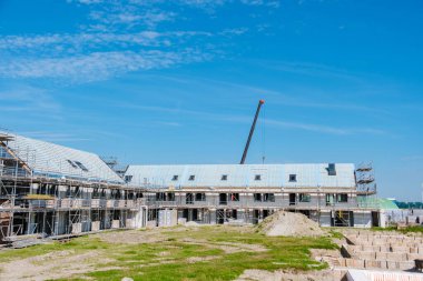 Yeni inşa edilmiş modern aile evleri, Hollanda 'da açık mavi gökyüzü altında canlı bir mimari sergileyerek bir inşaat sahasının ortasında yükseliyor.