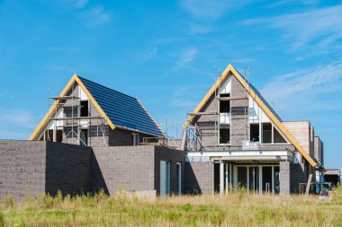 Yeni aile evleri, açık mavi gökyüzüne karşı modern mimari ve inşaat faaliyetlerinin sergilendiği canlı bir Hollanda banliyösünde ortaya çıkıyor. Hollanda 'da yeni evler inşa ediliyor