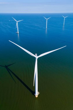 Uzun rüzgar türbinleri zarif bir şekilde dönerek Hollanda 'nın sakin sularında rüzgarı temiz enerjiye dönüştürüyor. Okyanustaki bir yel değirmeni parkının insansız hava aracı görüntüsü.