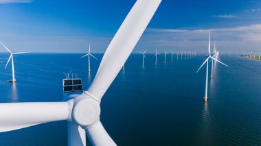 Sürdürülebilir enerjiyi kullanan rüzgar türbinleri mavi gökyüzüne karşı görkemli bir şekilde yükseliyor ve Hollanda 'nın yeşil teknolojiye olan bağlılığını gösteriyor. Okyanustaki bir yel değirmeni parkının insansız hava aracı görüntüsü.