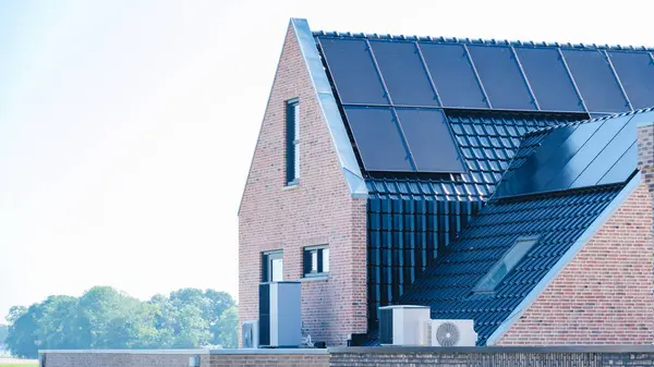 stock image A sleek air source heat pump enhances energy efficiency on a contemporary brick house, nestled in a lush green landscape in the Netherlands, warmte pomp translation air source heat pump