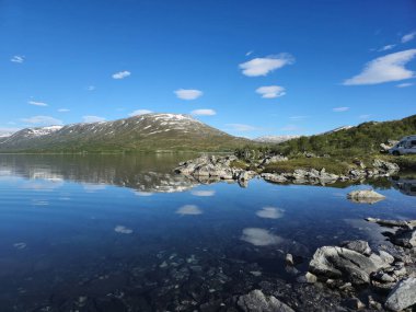 Norveç 'te nefes kesici bir yaz günüydü. Bakir dağlar, yemyeşil gölün etrafını saran sakin gölün güzelliğini yansıtıyordu..