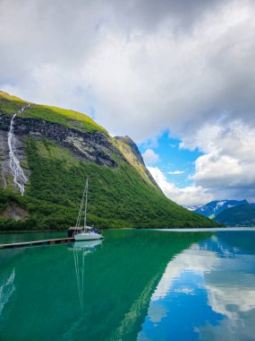 Bir yelkenli, Norveç 'in görkemli dağlarını ve yumuşak bulutlarını yansıtan ve doğanın zamansız güzelliğini gösteren canlı sularda sessizce dinlenir. Urke Köyü Norveç