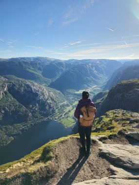 Yalnız bir yürüyüşçü kayalık çıkıntıda duruyor, aşağıdaki nefes kesici fiyorda bakıyor, sabah ışığında yıkanan yüksek dağlarla çevrili. Lysefjord Kjeragbolten Norveç