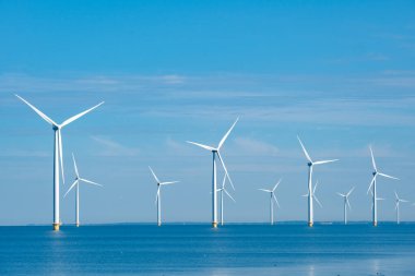 Uzun rüzgar türbinleri, sakin mavi suların üzerinde Hollanda 'daki parlak mavi gökyüzüne karşı yenilenebilir enerji üretiyor. Hollanda Noordoostpolder 'indeki Westermeerdijk yel değirmeni parkı