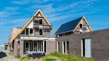 Hollanda 'nın bir banliyösünde yeni inşa edilmiş aile evleri, canlı mavi gökyüzüne karşı modern mimariyi sergiliyor. Hollanda 'da prefabrik ev