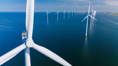 Görkemli rüzgar türbinleri Hollanda 'nın parıldayan sularının üzerinde dimdik durur ve berrak mavi gökyüzünün altında temiz enerji üretirler..