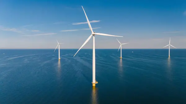 stock image Towering wind turbines spin gracefully in the open sea, harnessing renewable energy while the sky reflects a vibrant blue.