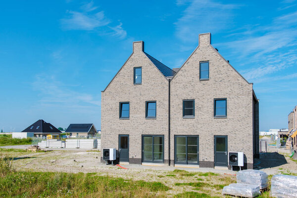 Two sleek air source heat pumps enhance the energy efficiency of a newly constructed duplex under a clear blue sky. warmte pomp translation air source heat pump