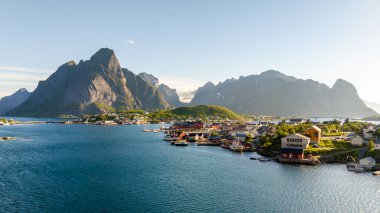 Altın sabah ışığı, yükselen dağlar ve sakin suların arasında yuva yapmış güzel bir sahil köyünü yıkıyor. Reine Lofoten Norveç