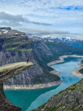 Soluk kesici bir uçurumun kenarında tek başına duran bir yürüyüşçü Norveç 'teki görkemli dağlarla çevrili bir fiyordun turkuaz sularına bakıyor. Trolltunga, Norveç